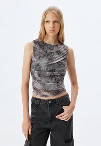 Top sin mangas en estampado de serpiente negro y gris, con un diseño fruncido y cuello redondo. Combinado con pantalones cargo negros de cintura alta.