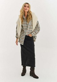 Košile se vzorem kostky v odstínech šedé, zelené a hnědé, vrstvená s krémovou načechranou vestou; doplněná černou džínovou sukní a hnědými kotníkovými botami na podpatku.