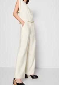 Ivoor mouwloos topje gecombineerd met losse, gestructureerde broek met elastische tailleband. Draag het met zwarte platformhakken.