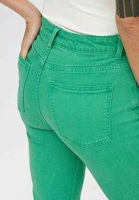 Green denim jeans with a fitted design, high waist, and two back pockets. Smooth texture with visible stitching details.