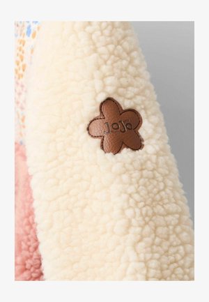 Povširana jakna v kremni barvi, z teksturirano površino. Okrašena z rjavim usnjenim označevalnikom v obliki cveta na rokavu.