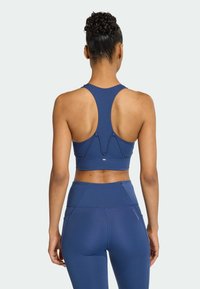 Tmavě modrá sportovní podprsenka s designem racerback, zdobená šitími a texturovaným povrchem. Legíny s vysokým pasem a bočními kapsami.