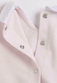 Vêtement pour bébé rose clair avec col blanc et boutons-pression argentés partiellement fermés sur un tissu doux.