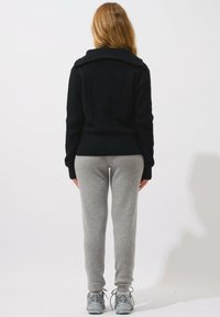 Svart stickad tröja med stor krage och diamantmönster på baksidan, tillsammans med grå sweatshirtbyxor och grå sneakers.