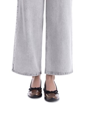 Bailarinas negras y marrones con un acabado texturizado brillante, que presentan un lazo en la parte delantera. Combinadas con pantalones de pierna ancha grises.