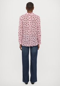 Long-sleeve pink blouse with red leaf print, buttoned back, paired with wide-leg dark jeans. Fabric appears lightweight and smooth.