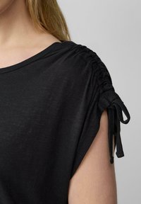 Zwarte top met korte mouwen en geplooide schouderdetails, voorzien van strikjes bij de mouwen en een zachte, gestructureerde stof.