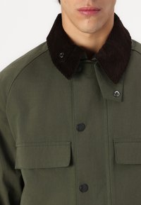 Olive green jacket with a brown corduroy collar, featuring snap buttons and two front pockets. Material has a smooth texture.