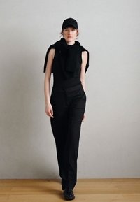 Fekete, testhez simuló felső, vállra vetett kötött sállal, hozzáillő, szűkített fekete nadrággal és fekete tornacipővel. Egyszerű, minimalista kialakítás.