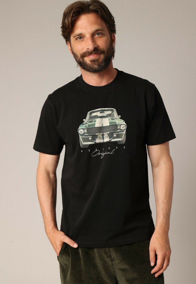 T-shirt en coton noir avec un graphique sur le devant d'une voiture vintage verte et des rayures blanches, portant le texte "DEELUXE Original" en dessous.