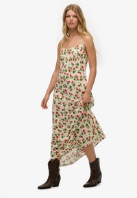 Satin maxi kjole med en cremefarvet baggrund, rødt blomsterprint, tynde stropper og en flydende kant. Sammen med brune hælede cowboystøvler.