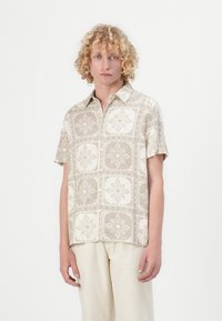Kortslepet skjorte i et lyst beige stoff, med et gjentatt blomstermønster og geometrisk mønster i krem, med krage som kneppes ned og avslappet passform.