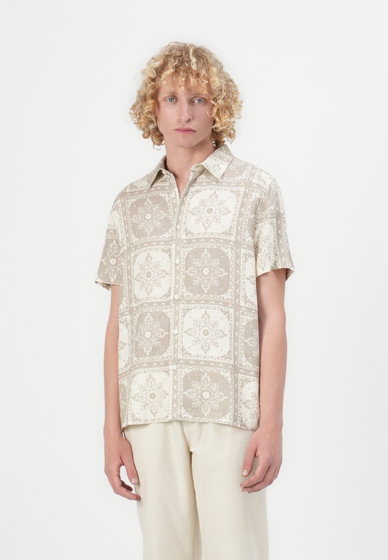 Kortslepet skjorte i et lyst beige stoff, med et gjentatt blomstermønster og geometrisk mønster i krem, med krage som kneppes ned og avslappet passform.