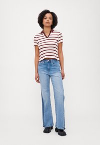 Kortermet, cropped, hvit og maroon stripet strikket topp med V-hals og burgunder krage, parret med lyseblå vide jeans og svarte støvler.