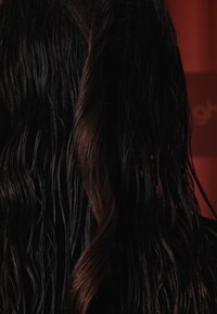 Långt, vågigt hår med en blandning av svarta och bruna nyanser, med definierade lockar och en texturerad framtoning mot en röd bakgrund.