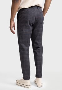 Pantaloni a quadri blu scuro con dettagli marroni, dotati di tasche e vestibilità su misura, abbinati a sneakers alte di colore chiaro.