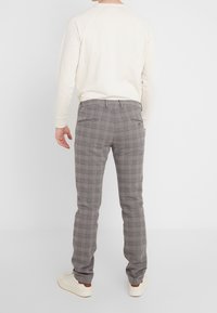 Grå rutiga byxor har en smal passform, knäppta bakfickor och en vävd textur, vilket kombineras med en krämfärgad sweatshirt och vita sneakers.