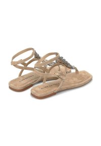 Beige suède sandalen met meerdere kruislings geplaatste banden, versierd met decoratieve metalen accenten, en een platte zool ontworpen voor casual gebruik.