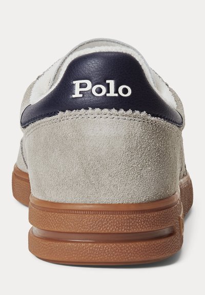 Szürke velúr tornacipő barna gumitalppal és tengerészkék bőr sarokfüllel, amelyen fehér "Polo" márkajelzés látható, hátulnézetből.