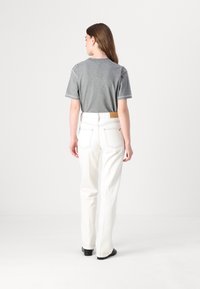 Grå kortärmad t-shirt som matchas med högmidjade vita jeans, med en läderlapp på midjebandet och minimal dekorativ sömnad.
