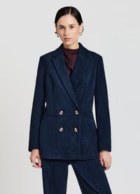 Blazer doppiopetto in velluto a coste blu navy con revers, caratterizzato da bottoni dorati e una silhouette strutturata, abbinato a pantaloni coordinati.