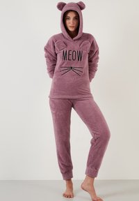 Set de loungewear roz cu blăniță, cu glugă și urechi de pisică. Partea de sus are textul "MEOW" și grafica mustăților, fiind completată de pantaloni asortați.