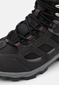 Botte de randonnée noire avec des lacets noirs à surpiqûres roses, des panneaux en mesh et en suède, et une semelle grise robuste sur fond blanc.