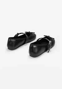 Des ballerines noires, en cuir lisse, avec un bout arrondi, une bride de cheville et un petit nœud décoratif à l'avant.