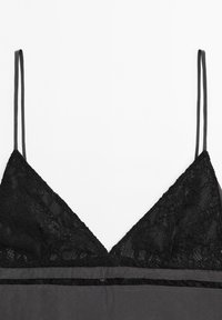 Black lace camisole with thin straps, featuring a deep V-neckline and a smooth fabric trim along the bottom for contrast.