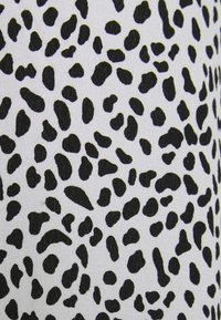 Gros plan d’un tissu avec des taches noires irrégulières sur un fond blanc, ressemblant à un motif dalmatien ou léopard.