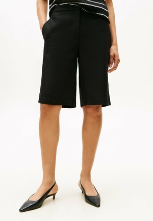 Schwarze Leinen-Shorts mit entspannter Passform, in der Mitte des Oberschenkels, seitlichen Taschen und flachem Frontdesign, kombiniert mit spitz zulaufenden Slingback-Absätzen.