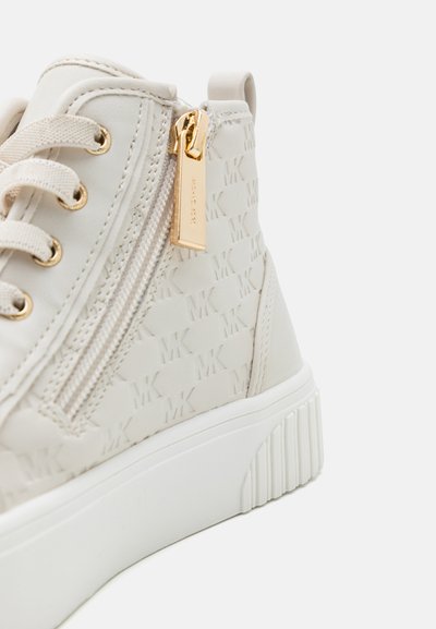 Beige Sneaker mit strukturiertem MK-Muster, goldener Reißverschluss, Schnürverschluss und einer weißen Plattformsohle mit gerippten Akzenten.