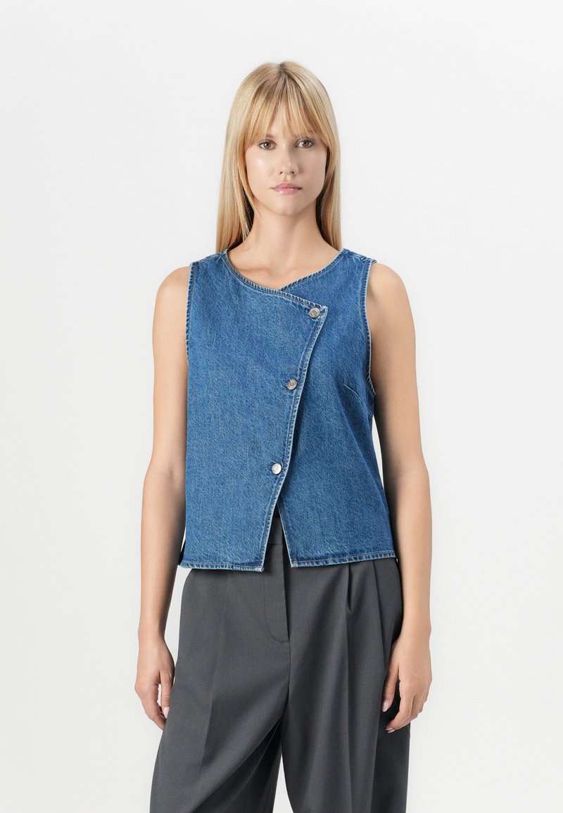 Denim vest in medium blue met een iets asymmetrisch ontwerp, ronde halslijn en zilveren knoopsluiting. Glad textuur, mouwloos stijl.