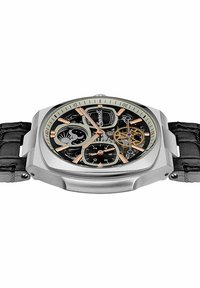 Silberner Edelstahlchronograph mit einem abgerundeten quadratischen Gehäuse, schwarzem Skelettzifferblatt, goldfarbenen Akzenten, schwarzem Lederarmband und sichtbarem mechanischem Uhrwerk.