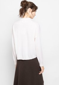 Maglione lavorato a maglia rosa chiaro con orlo corto e maniche lunghe, dotato di un colletto a coste. Indossato sopra una gonna marrone scuro.