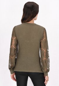 Top tricotat de culoare verde măsliniu, cu mâneci lungi din material transparent, având modele florale din dantelă. Material texturat, cu o croială lejeră și guler rotund.
