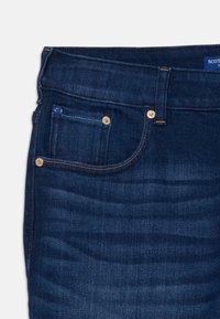 Donkerblauwe denim jeans met een klassieke snit, voorzien van een klein voorvak, messing knoopsluitingen en contrasterende oranje stiksels.