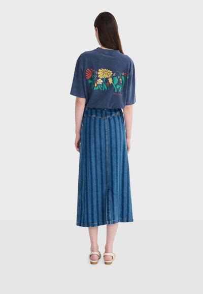 Woman standing facing away wearing a navy blue t-shirt with colorful floral print and a high-waisted, mid-length blue denim skirt.