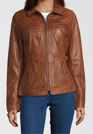 Brun tætsiddende læderjakke med lynlåslukning foran, bryst- og hofteer med lynlås, båret over hvid top og blå jeans.