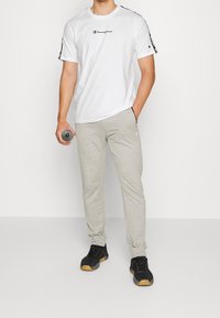 Hvid t-shirt med korte ærmer og sort logo, parret med lysegrå joggers med sidelommer, båret med sorte sportssko.