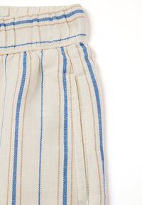 Tissu de couleur claire avec des rayures verticales bleues et beiges, doté d'une taille élastique et de poches latérales. Texture lisse.