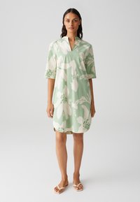 Short-sleeve dress in light green fabric featuring large white floral patterns with green accents; collarless design and straight cut.