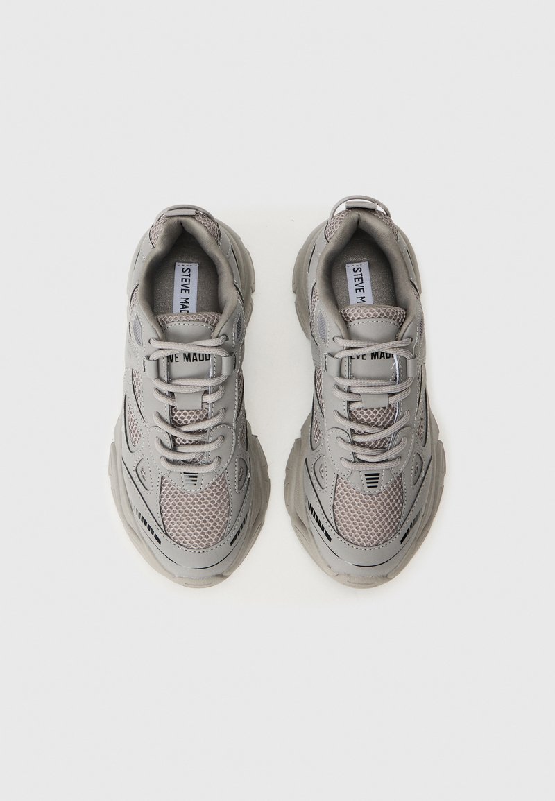 Un paio di sneakers grigie in materiale mesh e sintetico con suole spesse e stringhe, viste dall'alto su uno sfondo bianco semplice.