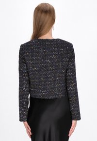 Jachetă cropped cu mâneci lungi, realizată dintr-un material texturat negru, cu fire multicolore și decolteu rotund. Fustă neagră din satin neted.