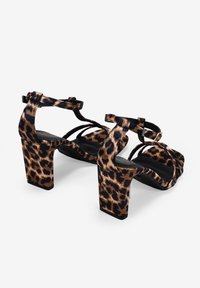Sandali con tacco alto in stampa leopardata, con cinturini neri, tacco a blocco e design con punta aperta. Il tessuto ha una consistenza liscia con una leggera lucentezza.