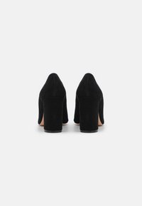 Chaussures à talons hauts en suédine noire avec un talon épais, bout pointu et texture lisse, vues de l'arrière.