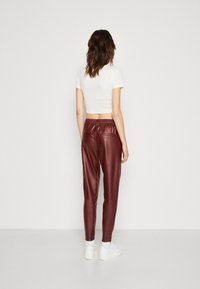 Pantalon en similicuir bordeaux avec une taille élastique, des poches latérales et une coupe fuselée, assorti à un crop top blanc ajusté et des baskets blanches.
