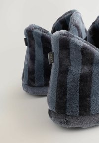 Blå og grå stribede plys-sandaler med en blød tekstur, rundede design og et lille mærke med "NEXT" på siden.
