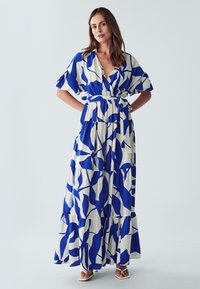 Mekko, jossa on V-aukko ja lyhyet hihat. Valmistettu kankaasta, jossa on sinivalkoinen abstrakti lehtikuosi. Kerroksellinen malli, jossa on vyö vyötäröllä.