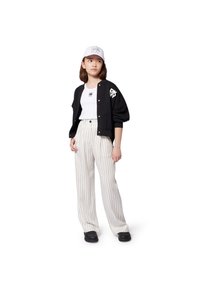Giubbotto bomber nero con logo DKNY, t-shirt bianca, pantaloni a palazzo beige a righe, e cappellino bianco con logo DKNY e visiera anteriore. Scarpe nere.